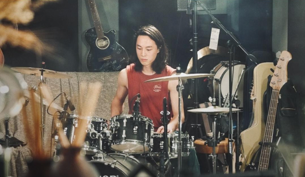 Mica Kim '28 sits in front of a drum set.