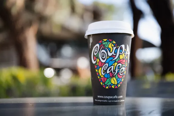 A cup of Coupa Cafe coffee sits in the foreground on a table outside Green Library.