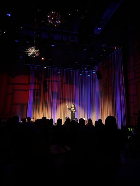 A woman stands onstage reading poetry.