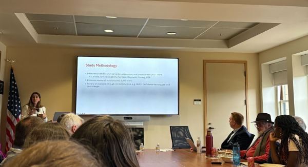 Rachel George lectures in front of people seated at a conference table.
