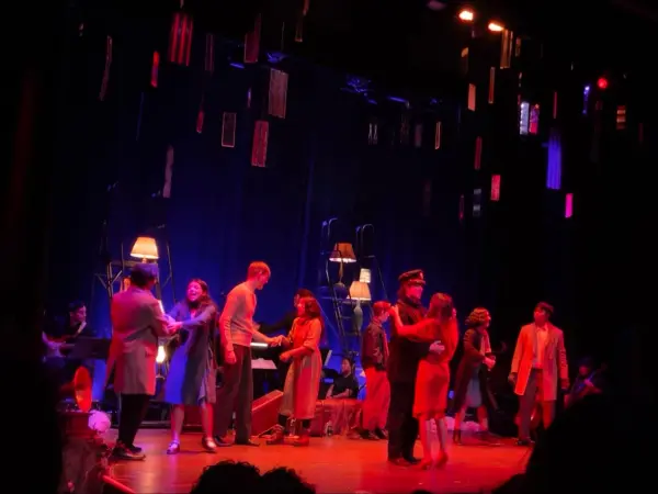 Stanford students sing and dance on the Piggott Theatre stage, bathed in red lights.