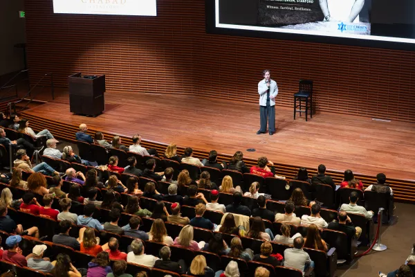 Omer Shem Tov stands on a stage, addressing a crowd of students