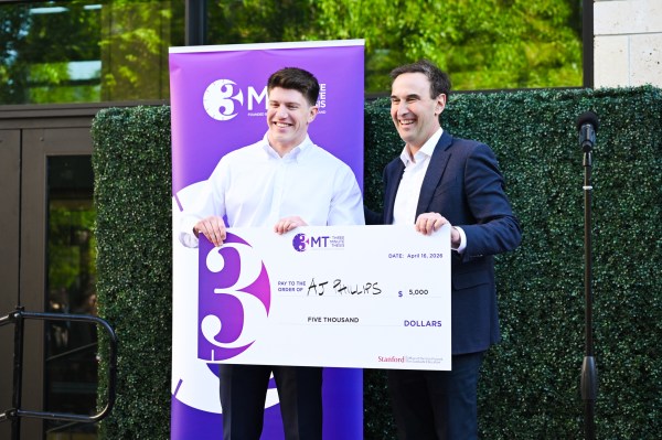 Ph.D. candidate AJ Phillips receives a $5,000 check from Stanford University President Jonathan Levin with purple 3 Minute Thesis Competition posters in the background.