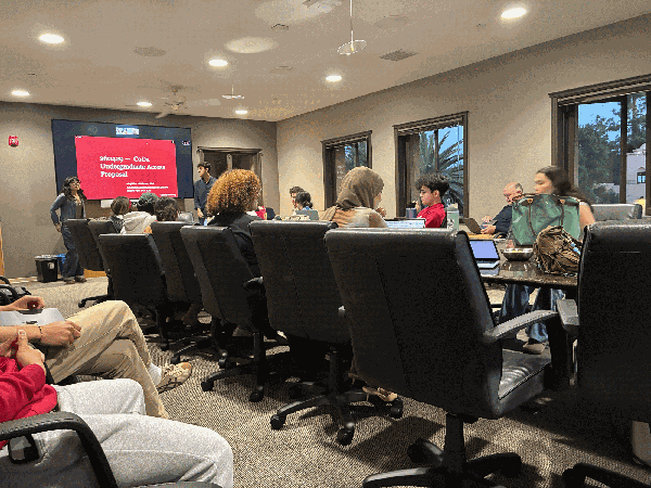 UGS senators sit around a conference table as two students give a presentation.