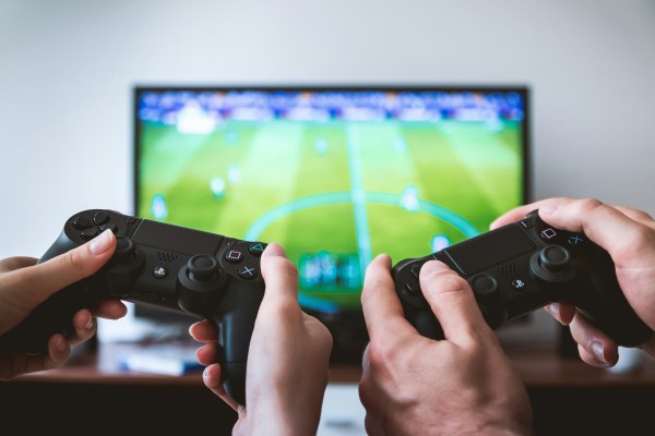Two hands holding up controllers in front of a soccer (football) video game.
