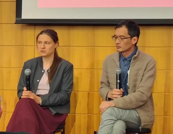 Two people sit on a panel holding microphones.