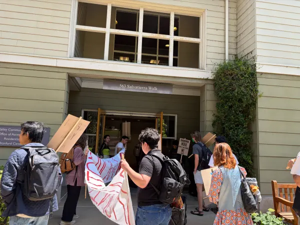 Students gather with signs in front of a white and grey building,