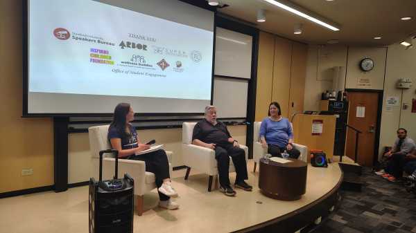 Panelists sit in armchairs on a wood-paneled stage.