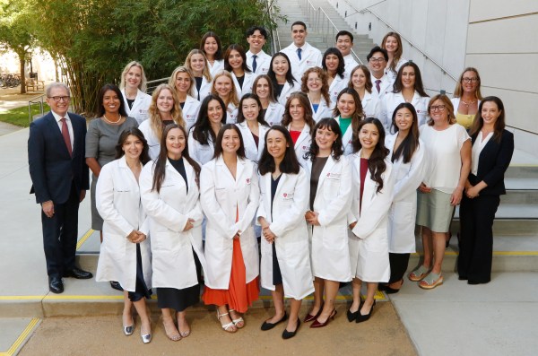 A large group of medical students poses for a photo in their white coats.