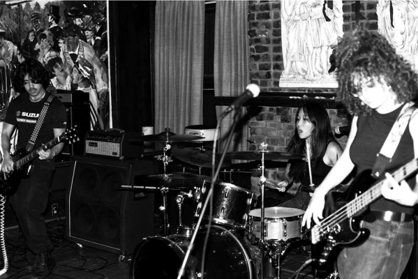 A monochromatic photo of two guitar players and a drum player performing