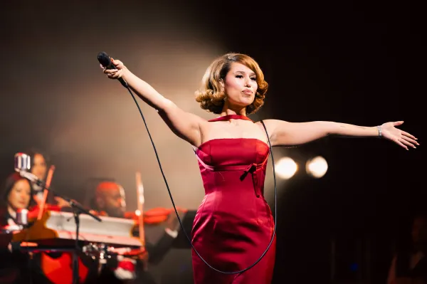 Raye holds a microphone in a red gown as she performs onstage.