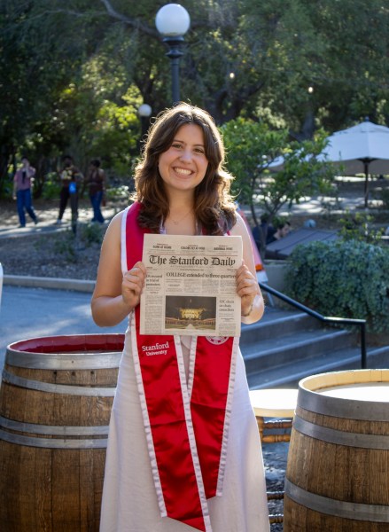 Greta Reich in graduation garb holding an issue of the Daily