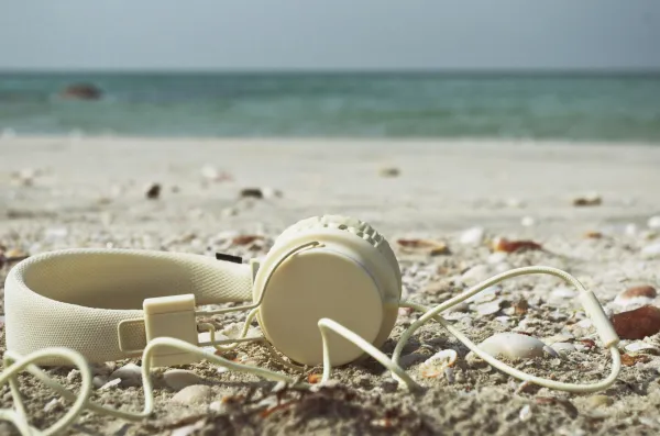 A pair of white headphones laid on the sand at the beach