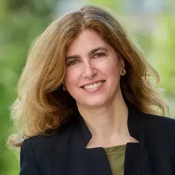 A woman with brown hair and a black outfit smiles at the camera.