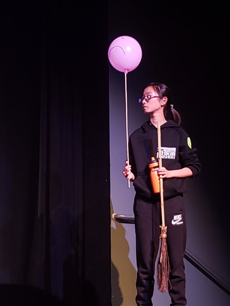 Alaina on the side of a stage, holding a pink balloon with an unhappy face