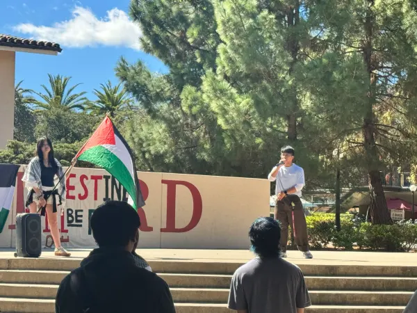 Two people onstage at White Plaza, one holding a Palestinian flag.