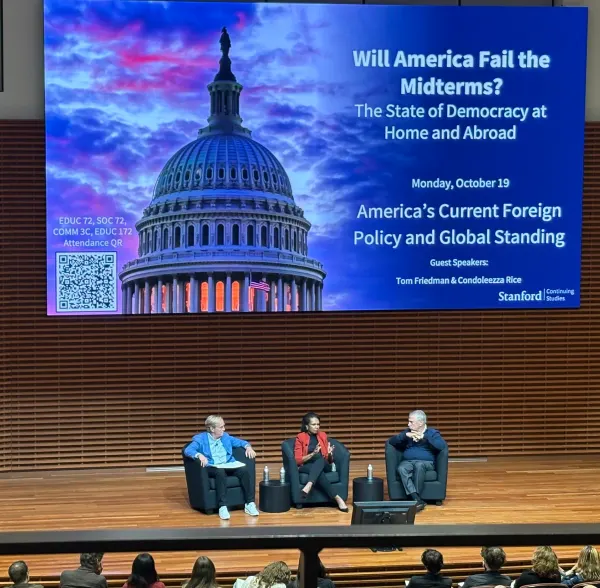 Three speakers sit on stage in front of big screen.