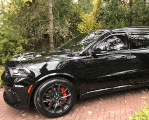 A black car parked with trees in the background.